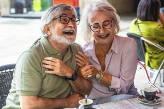 Mature couple laughing and chatting over coffee on a sunny outdoor cafe patio, enjoying relaxed