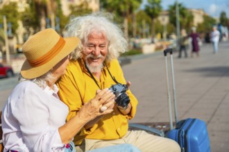 Happy senior couple sitting on a bench in a sunny european city, smiling as they examine a vintage