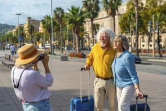 Senior friends traveling together, posing for a picture with luggage on a sunny city street,