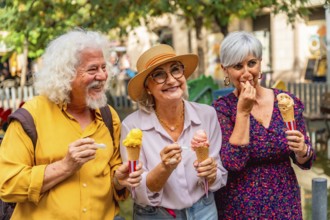 Three happy senior friends, two women and one man, standing outdoors and enjoying colorful ice