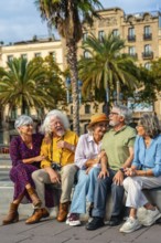 Group of happy senior friends smiling and interacting while sitting on a bench in a city square,