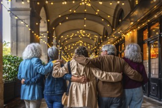 Group of diverse senior friends walking together embraced along an illuminated city archway at