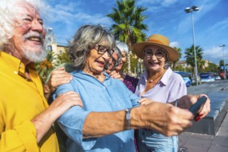 Group of smiling seniors enjoying a vacation, standing outdoors together and using a smartphone to