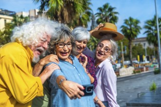 Group of four joyful senior friends laughing and smiling while capturing a memorable selfie with a