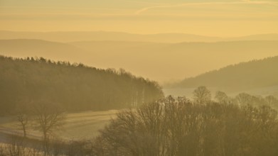 Blurred hills and golden sky at sunrise create a misty, quiet landscape, Seckmauern, Lützelbach,