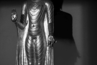 Standing gilded Buddha statue, right hand (raised, open palm outwards) symbolizes the Abhaya mudra,