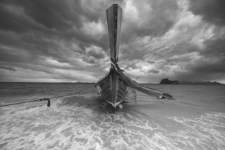 Longtail boat on the beach with dark rain clouds behind it, Koh Ngai island, Andaman Sea, Satun