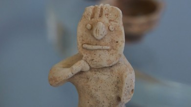 Figurine of a boy holding a mask in front of his face, ancient clay figure with simple facial