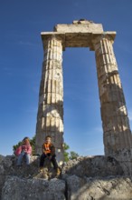 Two children sit in front of an ancient column. Clear Sky, Nemea, Ancient Zeusheightum,