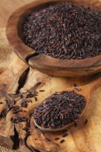 Natural black rice in a wooden bowl and spoon on a wooden surface in rustic style, top view