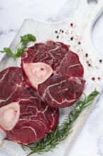 Knuckle on the bone, raw meat for ossobuco, on a wooden chopping board, with a sprig of rosemary,