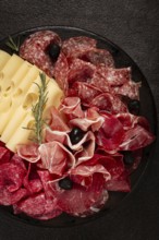 Cold cuts, appetizer, prosciutto, salami and ham, with maasdam cheese and olives, on a round plate,