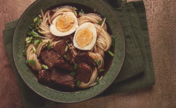 Asian noodles in broth, with beef and egg, top view, close-up, no people