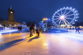 Skaters in front of the Red Town Hall, Neptune Fountain and a Ferris wheel at the Berlin Christmas