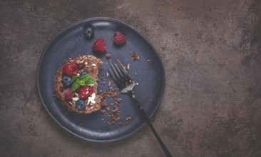 Half-eaten chocolate tartlet, on a plate, stuffed with cottage cheese and berries, breakfast,
