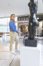 A woman stands in front of a sculpture in a bright museum room, robotic personality Roboloutions in