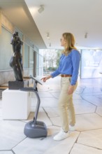 Woman using a device in front of a statue in a modern museum, robotic personality Roboloutions in