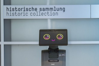 A cute robot with a smiley face in front of a sign with the inscription 'historical collection',