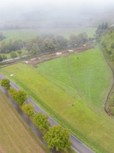 Aerial view of a green landscape with trees and a construction site along a road, Bau PV