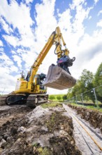 An excavator carries out earthworks on a construction site under a cloudy sky, Bau PV