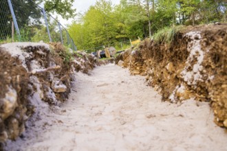 An excavated ditch with soil and sand on a construction site surrounded by vegetation, construction