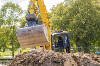 An excavator on a construction site lifts soil near trees and a cloudy sky, building a PV open air