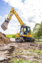 A yellow excavator picks up soil on a construction site under cloudy skies, Bau PV