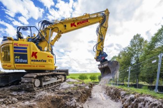 A yellow excavator digging on a construction site under a cloudy sky, Bau PV Freifaechenanlage,