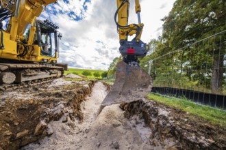 An excavator lifts soil from a deep ditch on a construction site in cloudy skies, construction PV