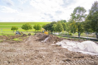 Extensive construction site with row of trees and machines in a rural landscape, construction of a