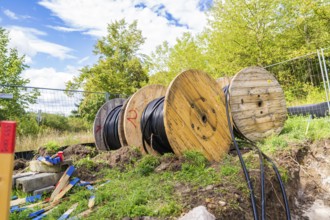 Several large cable drums with cables on a construction site in a green area, Bau PV