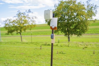 Camera on a post, surrounded by green fields and trees, against a cloudy sky, Bau PV