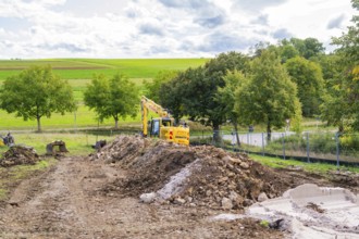 Excavator on a construction site with large mounds of soil in a green landscape, Bau PV
