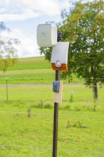 Camera mounted on a fence post in a rural landscape in front of a green field, Bau PV