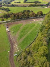 View of hilly landscape with a path surrounded by green fields and trees, construction PV
