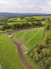 Extensive green landscape with trees, a path and rolling hills under cloudy sky, Bau PV