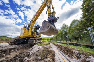 An excavator excavates a ditch in a natural environment under cloudy skies, Bau PV
