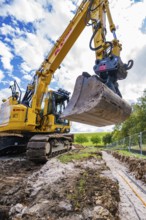 Large excavator digging a trench under cloudy sky, Bau PV Freifaechenanlage, Weil der Stadt,