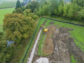 Excavator working on an earthen ditch in a green area, Bau PV Freifaechenanlage, Weil der Stadt,