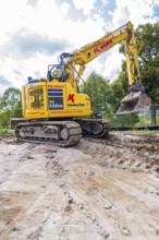 A yellow excavator doing earthwork on a construction site under cloudy skies, Bau PV
