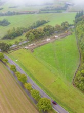 Aerial view of a vast green field with a construction site and road, PV Freifaechenanlage