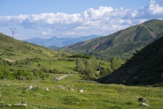 Valley with green landscape, power lines, surrounded by mountains and under a cloudy sky, landscape