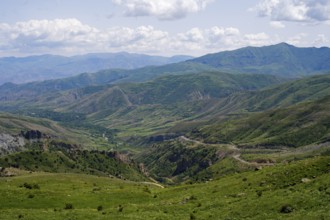 Rolling hills and mountains around a wide valley with green vegetation, cloudy sky, views from