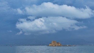 Bourtzi island fortress, a castle perched on a small island in blue water under a dramatic cloudy