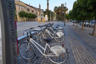 Old town of Nauplion, bicycles on a paved town square with historic buildings and palm trees,
