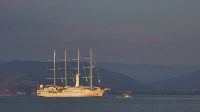 An illuminated sailing ship on calm water with mountains in the background at dusk, Nauplion,