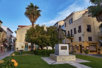 Old town of Nauplion, statue on a green area surrounded by buildings and palm trees under a clear