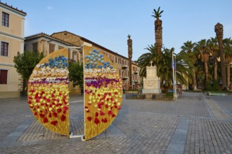 Old town of Nauplion, colorful flower installation on a town square with palm trees and monuments,