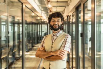 Young male business professional with curly hair and beard smiling for the camera while standing