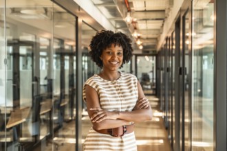 Young african american businesswoman smiling with crossed arms, standing confidently in a modern